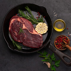 raw beef ribeye steak on black cast iron pan, ready to cook, black background , top view, square image