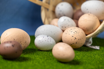 Speckled Eggs Spilled From A Wicker Basket Onto Green Grass With A Blue Background, Representing Easter, Farming, And Nature Concept