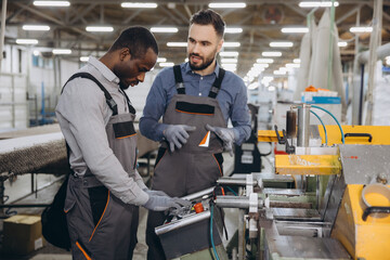 Two interracial factory male workers operating industrial machinery producing aluminum and PVC windows and doors