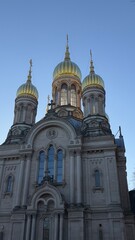 Detailed facade of an Orthodox church with stunning golden domes gleaming in the sunlight. The architecture features intricate ornaments, tall windows, and a central cross. Winter