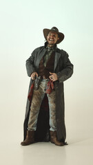 Portrait of cheerful man, cowboy with wide smile, wearing long coat, vest and hat, holding gun...