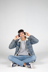 Chico joven vestido de vaqueros y camiseta blanca sujetando auriculares y mirando a un lado sonriendo. Fondo blanco. Concepto de música, tecnología y publicidad.