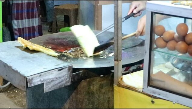 A vendor prepares an martabak telur or egg, an Indonesian specialty. Fried in hot oil on a flat pan.And use a spatula to cook .Focus on food.blurred,shake video,exposure,nighty noise