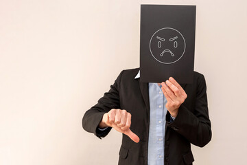 Businessperson hiding face with angry emoticon and showing thumbs down