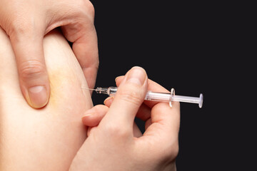 Close-up shot of injection to the abdomen with medical syringe, dark background
