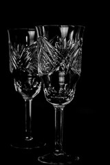 Intricately cut crystal wine glasses feature geometric patterns and a reflective surface, enhancing their transparency. The glasses have long stems and a tapered shape.