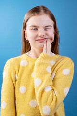 Playful girl in a yellow polka dot sweater making a funny face, pressing her cheek with one hand,...