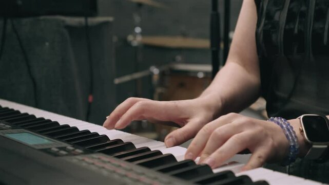 Musician hands pressing keys on electronic keyboard during recording session in studio. Background features blurred drum set, emphasizing focus on performance, creativity, and sound production.