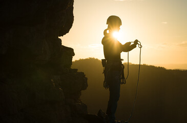 Young girl is preparing for training on the rocks sunset, in the mountains and puts a helmet on her...