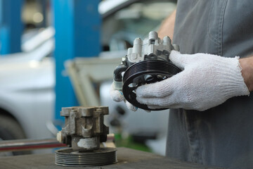 Car repair at a car service station.An auto mechanic is preparing to replace a faulty hydraulic power steering pump with a new one.