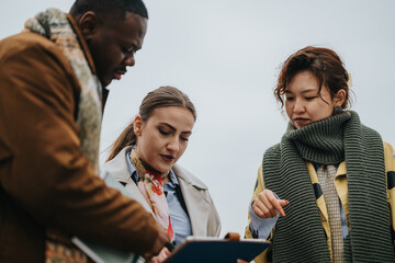 Three people engaged in a discussion outdoors, reviewing notes and ideas together. They appear focused and collaborative, working effectively as a team towards shared objectives.