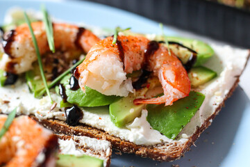 Delicious open-faced sandwich with creamy cheese, avocado, shrimp, and balsamic glaze on whole-grain bread. It is topped with sesame, smoked paprika, and wheat microgreens. A perfect seafood appetizer