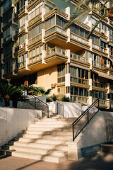 An outdoor staircase illuminated by sunlight with palm shadows on the steps, leading up to an apartment building facade