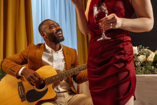 Musician playing acoustic guitar for elegant woman drinking wine - Powered by Adobe