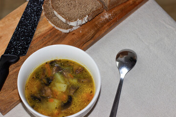 chicken and vegetable soup, Mushroom soup in a white bowl. nearby on a wooden board are sliced...
