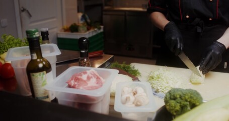 A woman in a chef's uniform with disposable black gloves on her hands cuts cabbage in the restaurant kitchen, close-up of her hands, no face