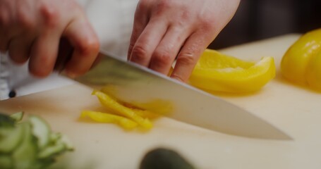 A man in a chef's uniform cuts a cucumber, a close-up of his hands