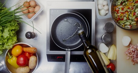 A woman with disposable black gloves on her hands pours oil on a frying pan standing on the stove,...
