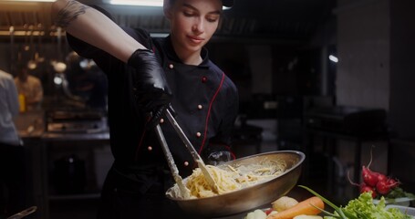 A woman in a chef's uniform puts ready-made pasta on a plate