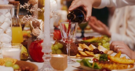 Guests smile and talk while sitting at a beautifully set festive table outdoors. A man pours wine into a glass
