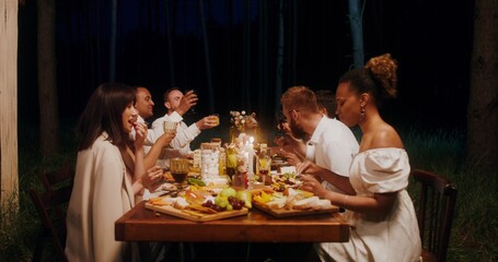 Guests smile and talk while eating sitting at a festive table outdoors at night