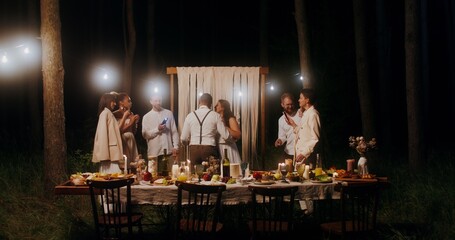 The bride and groom are dancing surrounded by their friends at an outdoor wedding feast at night