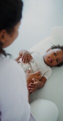 Mom and daughter of African-American appearance laugh and play together on the couch indoors, mom...