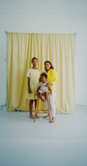 A mother with two children smiles while looking at the camera posing in the studio. The baby is fidgeting on the chair