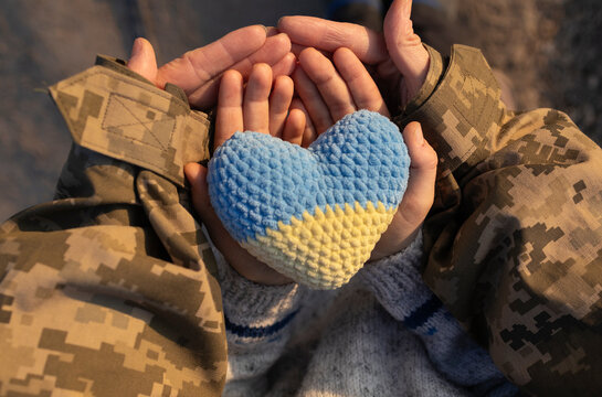 yellow-blue knitted heart in hands of a child and an adult in an army camouflage uniform. Defender of Ukraine Day. Independence Day. Faith in the Armed Forces. Support Ukraine in the war with Russia
