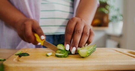 Women's hands are cutting a cucumber while preparing a salad in the kitchen, there is no face