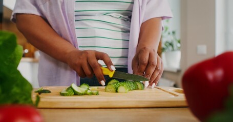 Women's hands are cutting a cucumber while preparing a salad in the kitchen, there is no face