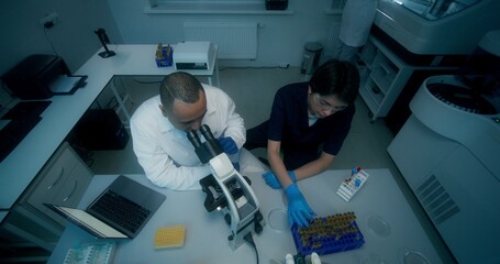 A man and a woman in lab coats are working in a medical laboratory, conducting a blood test and...