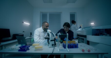 Naklejka premium A group of laboratory assistants in medical clothes work in a medical laboratory, using a microscope and conducting a blood test