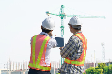 Construction engineers discuss building construction plans against the background of construction cranes.
