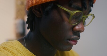 A man with glasses and a knitted hat is working sitting at a desk in the office, close-up of his focused face