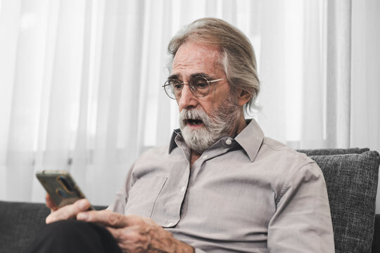 Senior Man Using Smartphone. 75 Years Old Gray Haired Western Man Sitting on Couch, Exploring Technology, Modern Apps, Digital Connection.