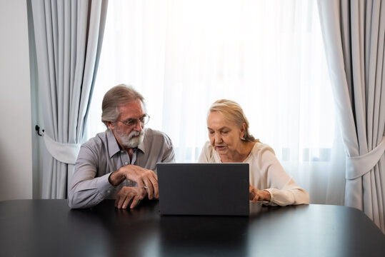 Happy Caucasian 70s mature couple using laptop at home. Old people using computer at home. Senior man and woman surfing the web on a wireless laptop connection. Modern retired lifestyle people.