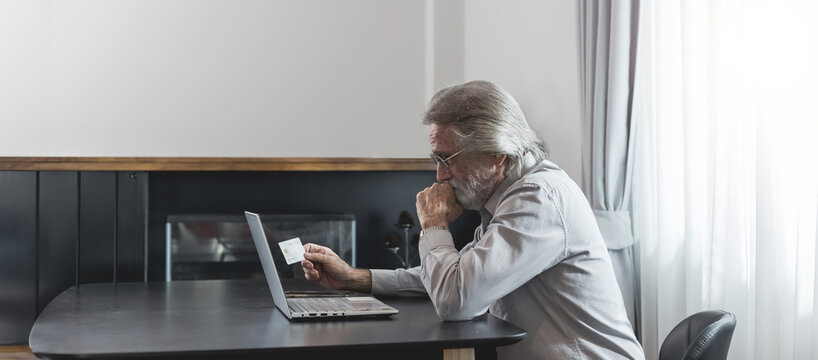 Upset senior elderly man holding credit card by laptop having trouble worry finance safety data or online payment security. Bank client concerned about problem with credit card, financial fraud threat