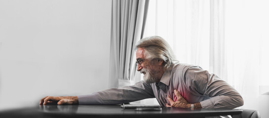 Senior man in spectacles presses hand to chest has heart attack suffers from unbearable chest pain closes eyes wears glasses sitting in front of laptop. People age and problems with health.