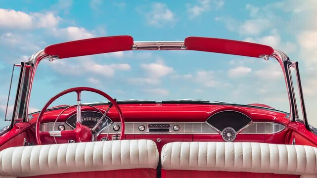 Driver view of a red vintage classic open American cabriolet car in front of a sunny blue sky