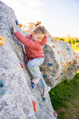 Little girl climbing an artificial climbing wall in a playground, developing strength and...