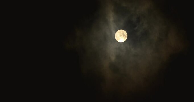 The full moon shines through the clouds in a dark night sky