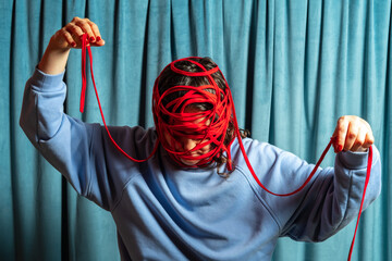 Woman in blue with her head tied with red threads against blue velvet curtains background . Mental problems concept.