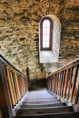 A staircase with a window in the middle. The window is small and has a wooden frame. The staircase is made of wood and is very narrow