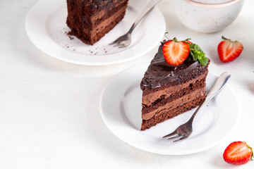 Dark chocolate cake slices, with chocolate cream and strawberry, on portioned plates, copy space