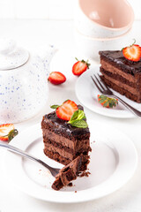 Dark chocolate cake slices, with chocolate cream and strawberry, on portioned plates, copy space