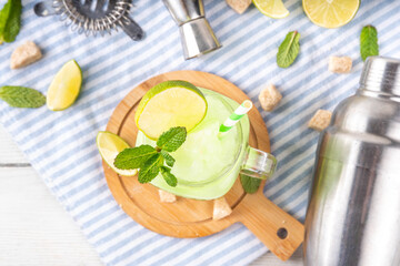 Mojito lemonade alcoholic slush cocktail, in a martini glass, summer refreshing slushy drink with vodka, lime juice and mint syrup, on a white table with bar utensils