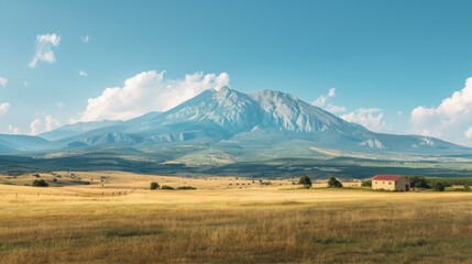 Expansive Field Leads to Dramatic Mountain Backdrop with Rustic Barn Under a Clear Blue Sky