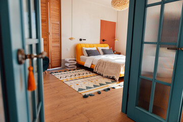 A cozy bedroom with white walls. An open stylish blue door. Wooden bed with stylish bedside tables...