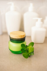 A close-up of a jar of green glass cream with a wooden lid and a twig with leaves. A mockup of a cosmetic product on the table.